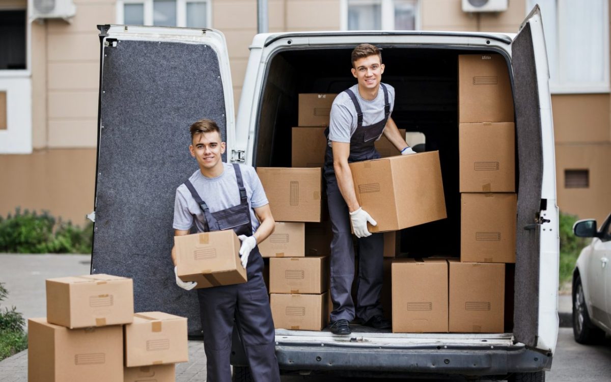 two-young-handsome-smiling-movers-wearing-uniforms-are-unloading-the-van-full-of-boxes-house-move.jpg