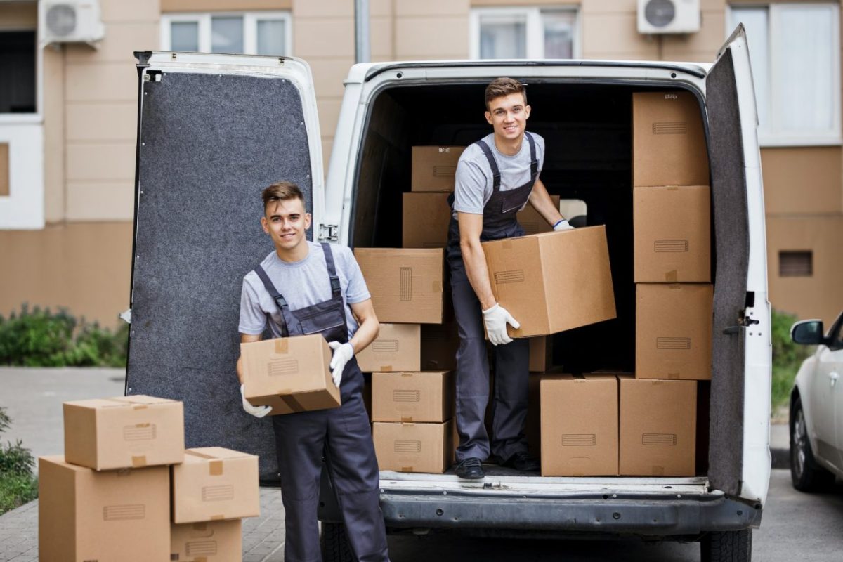 two-young-handsome-smiling-movers-wearing-uniforms-are-unloading-the-van-full-of-boxes-house-move.jpg